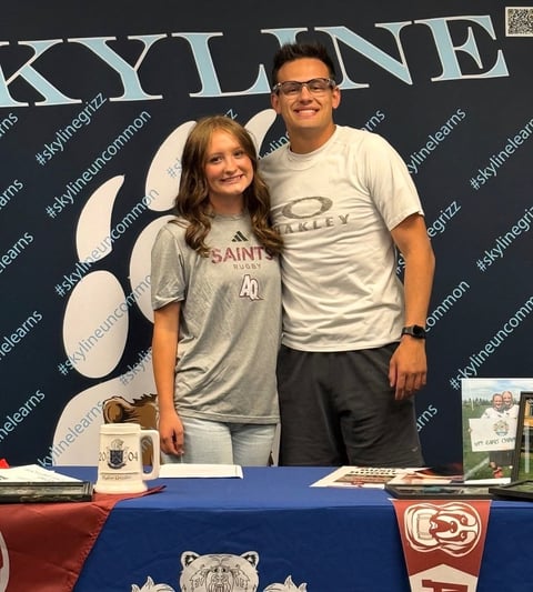 Man and young girl standing together at a table with Saints sports merchandise, posing in front of a Skyline backdrop