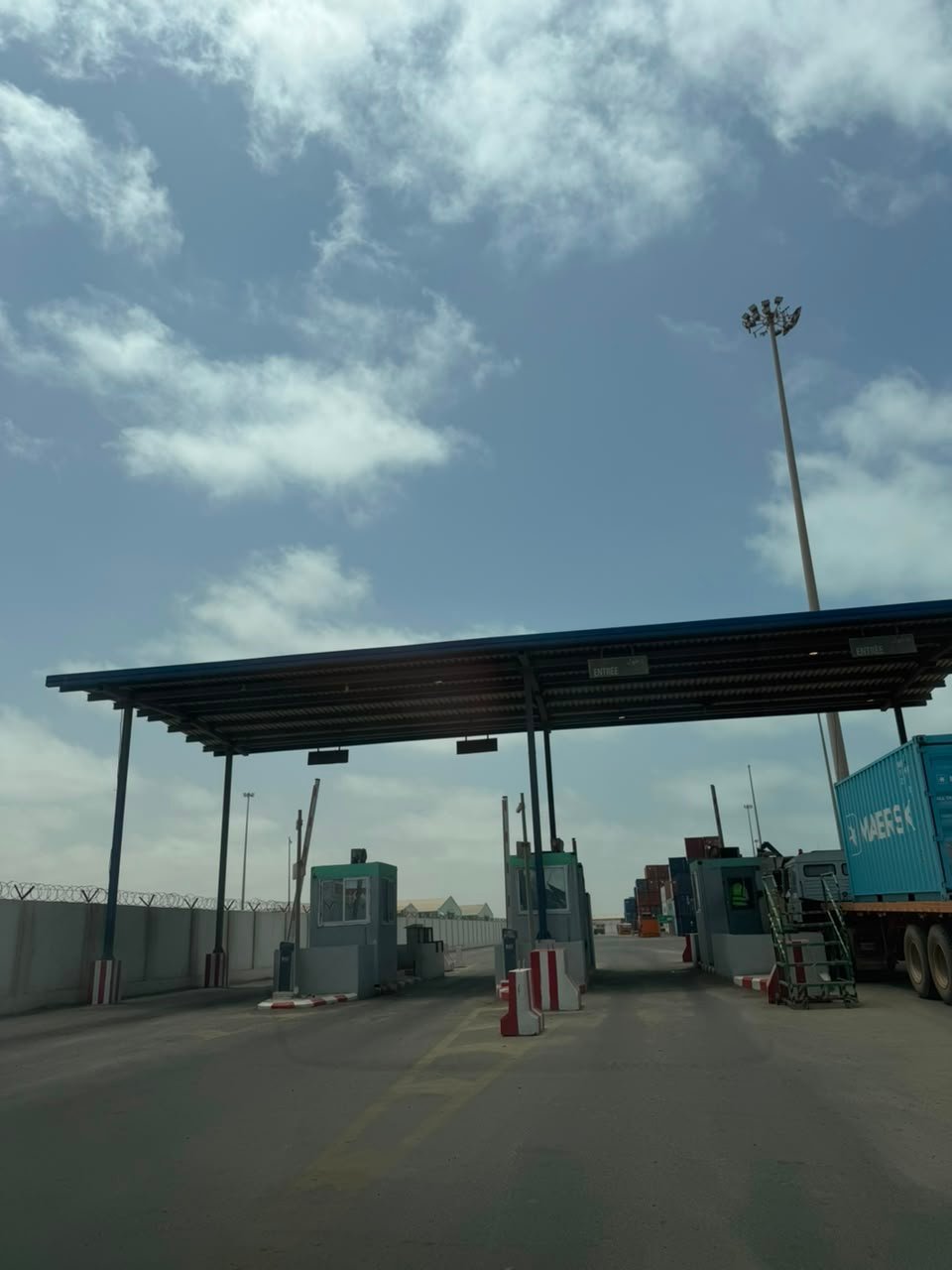 Toll booth checkpoint with metal canopy, toll collection booths, and trucks lined up under cloudy sky