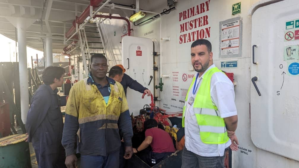 Workers in safety gear standing in an industrial muster station during a safety briefing or drill