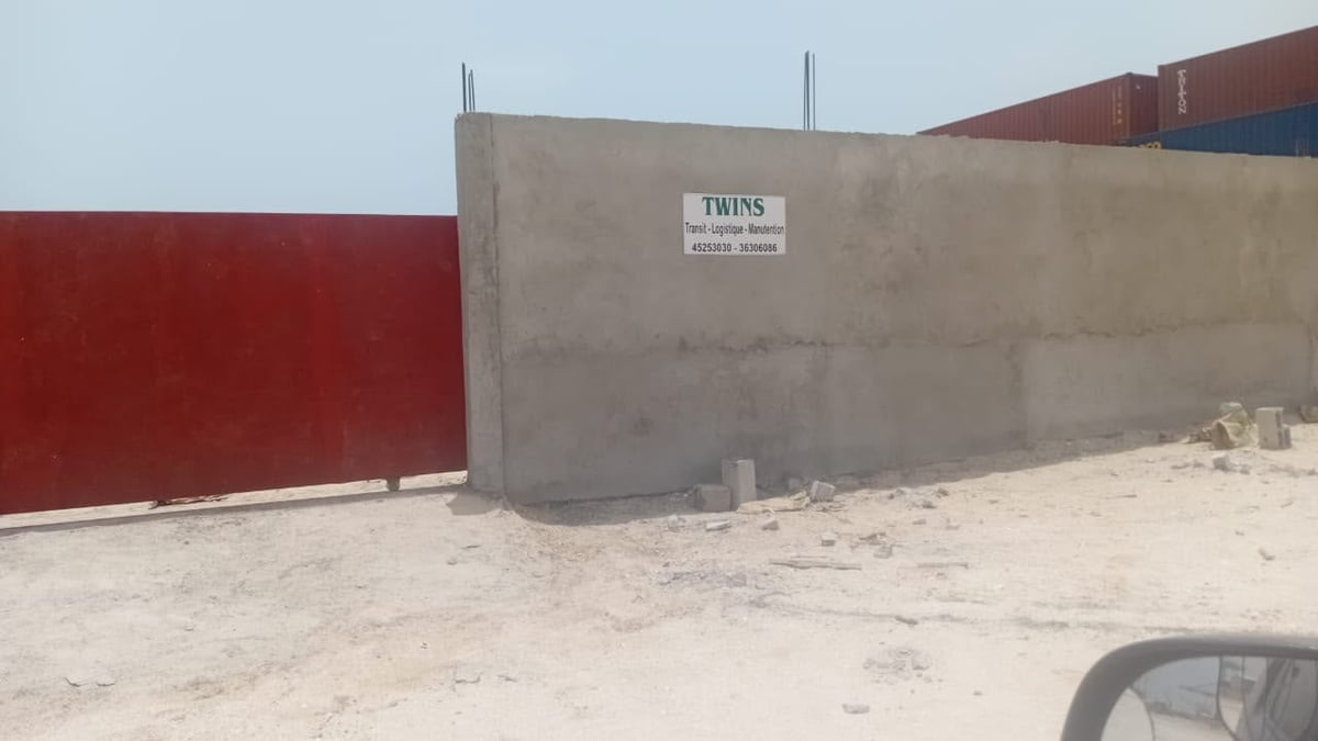 Construction site with concrete bunker structure and red metal wall on sandy ground at the Twins shipping facility