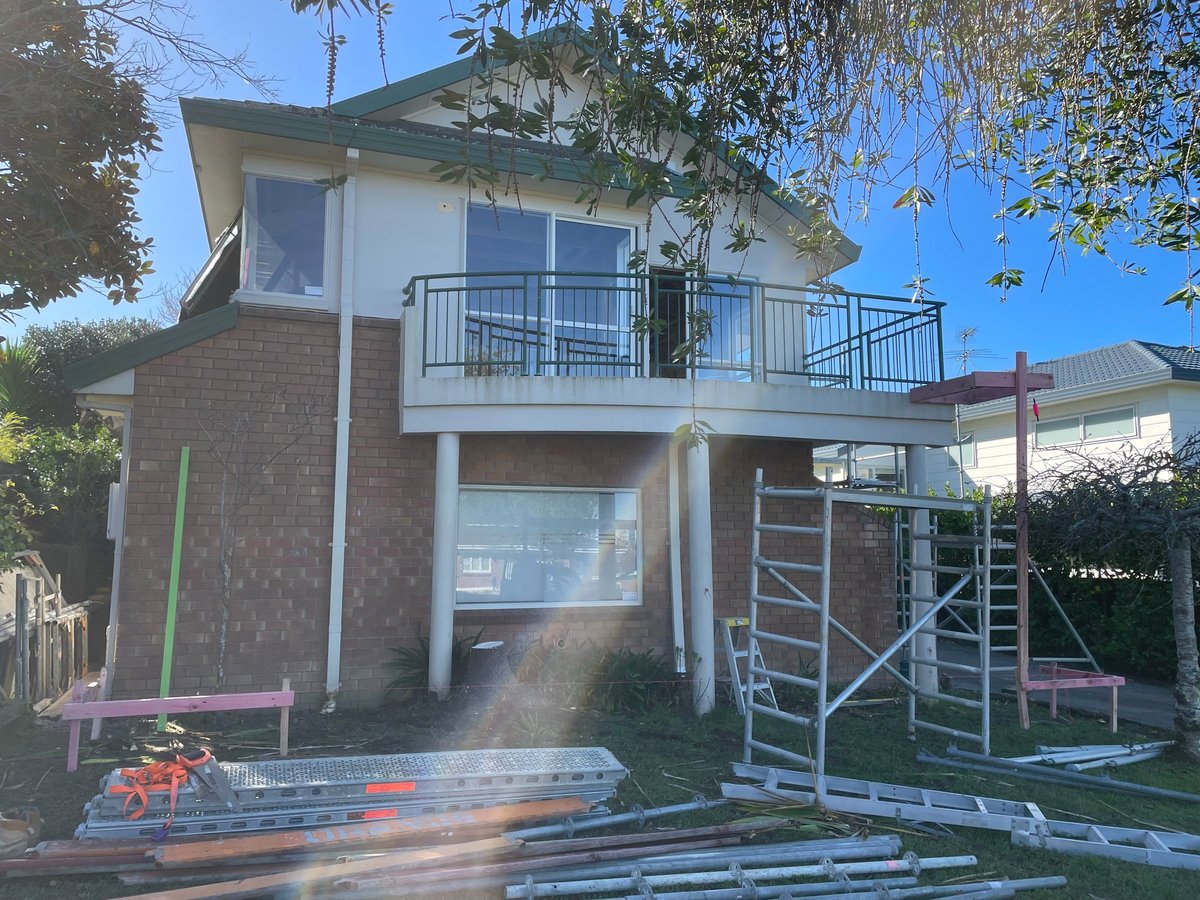 Two-storey brick and plaster Hauraki house with metal balcony and scaffolding, before the extension and reclad
