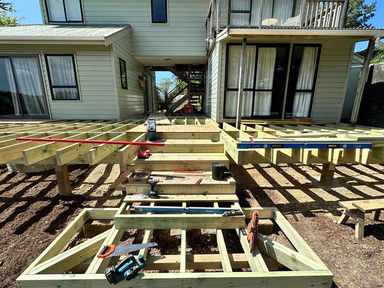 Construction of a wooden deck addition to a house with framing and joists visible, showing work in progress on multiple levels