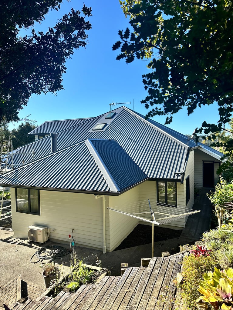 Modern cream and black house with metal roof surrounded by green trees and wooden deck