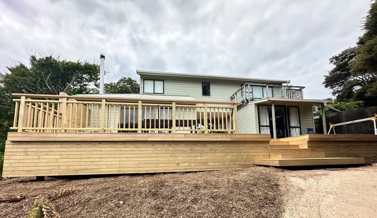 Modern two-story house with light green exterior and large wooden deck overlooking gravel yard on cloudy day