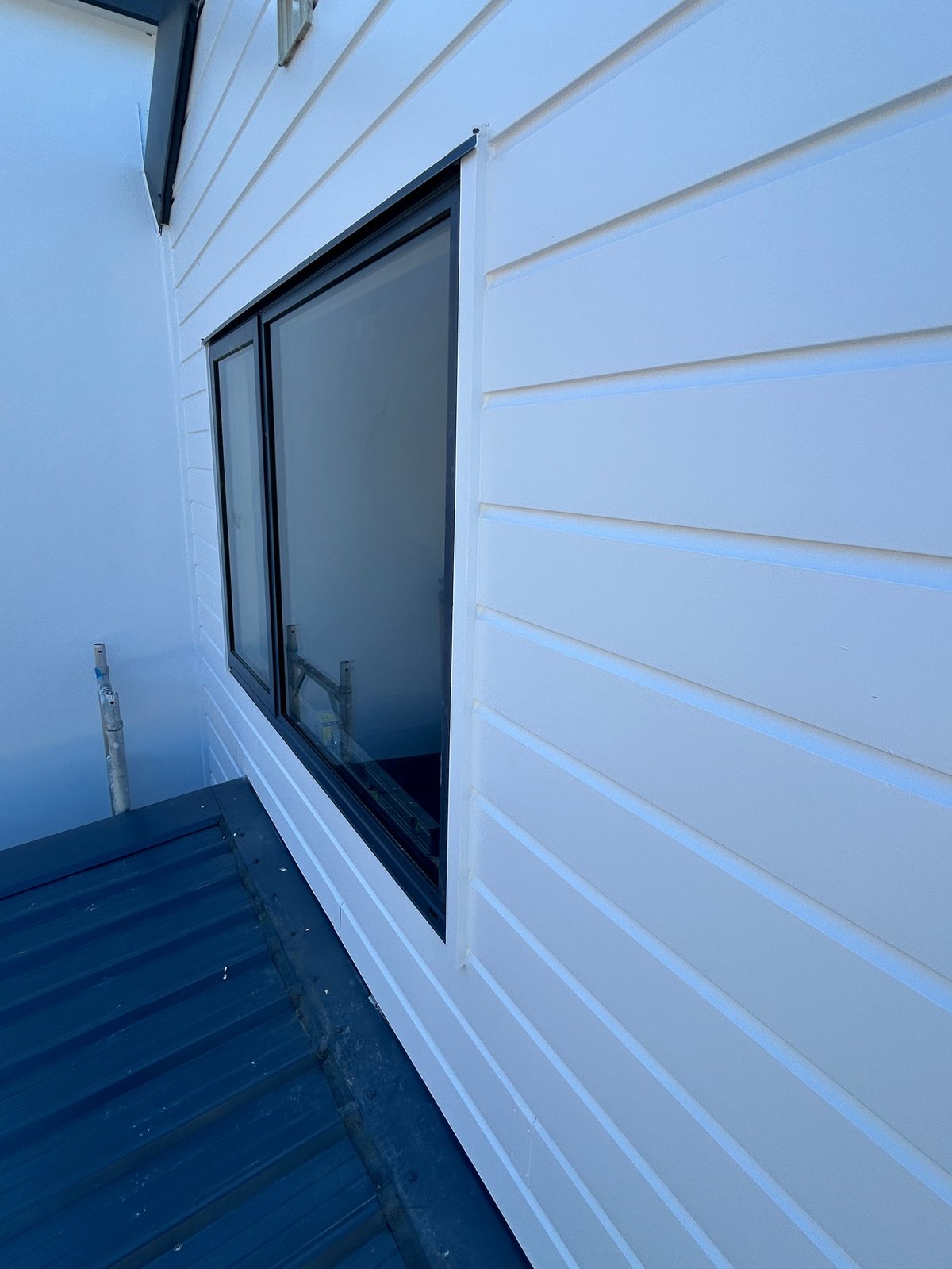Modern window with dark frame on white horizontal siding of residential building, viewed from corner angle