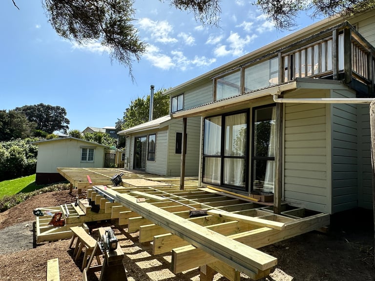 House renovation showing wooden deck framing under construction with modern extension and landscaped garden under clear blue sky