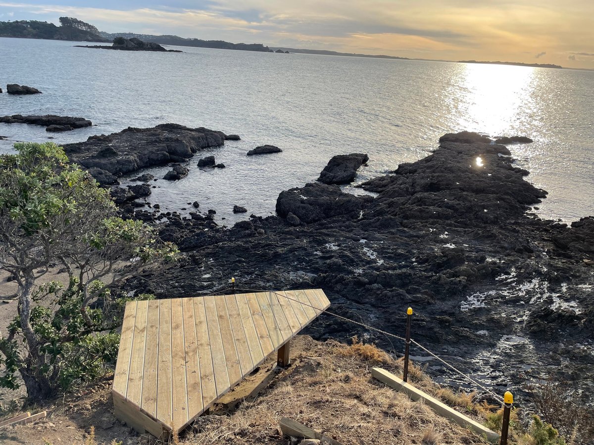 Finished wedge-shaped timber viewing platform at the rocks on Waiheke Island, at sunset over the bay