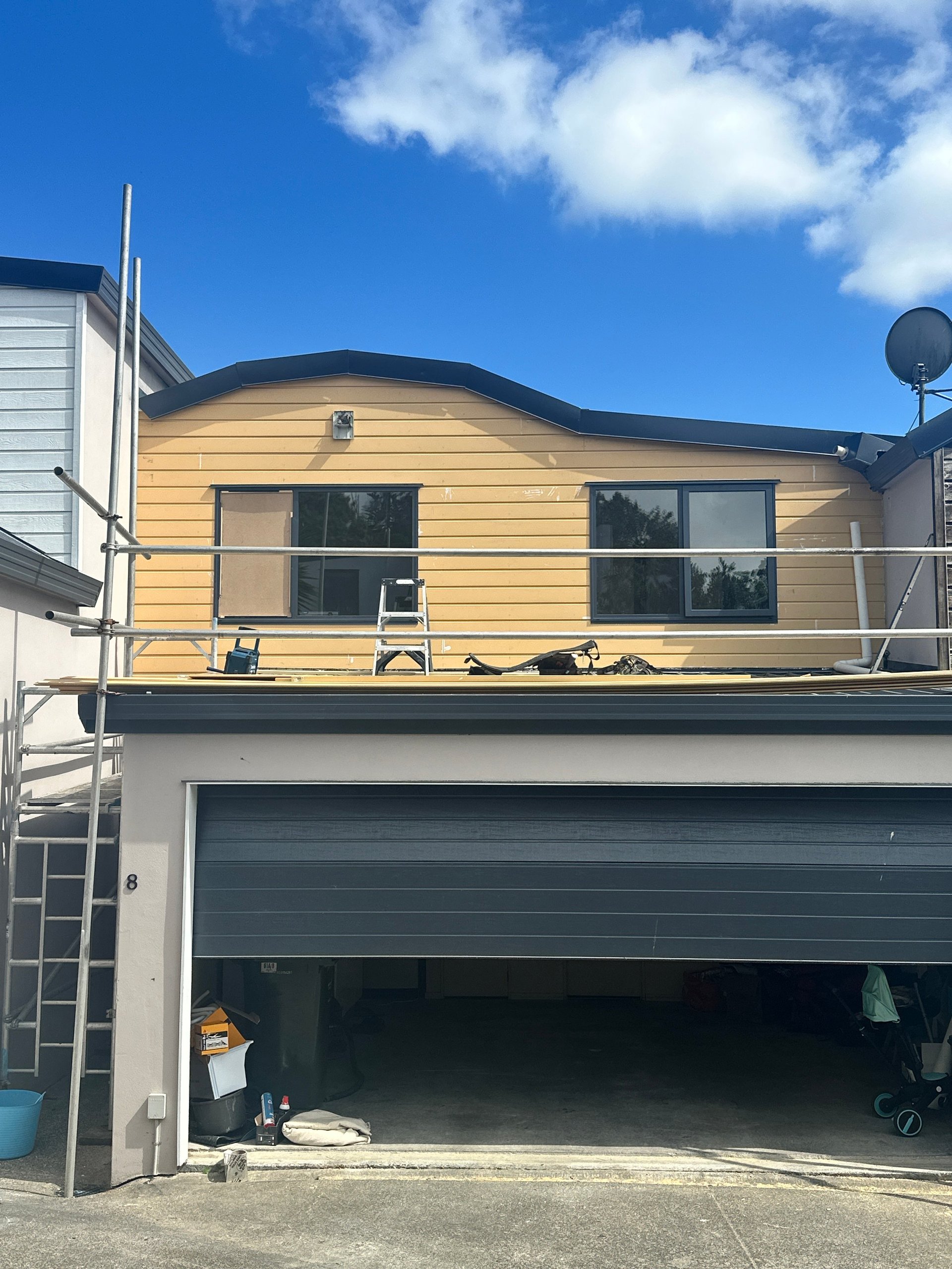 Modern two-story house with yellow siding, two-car garage, and blue sky with white clouds.