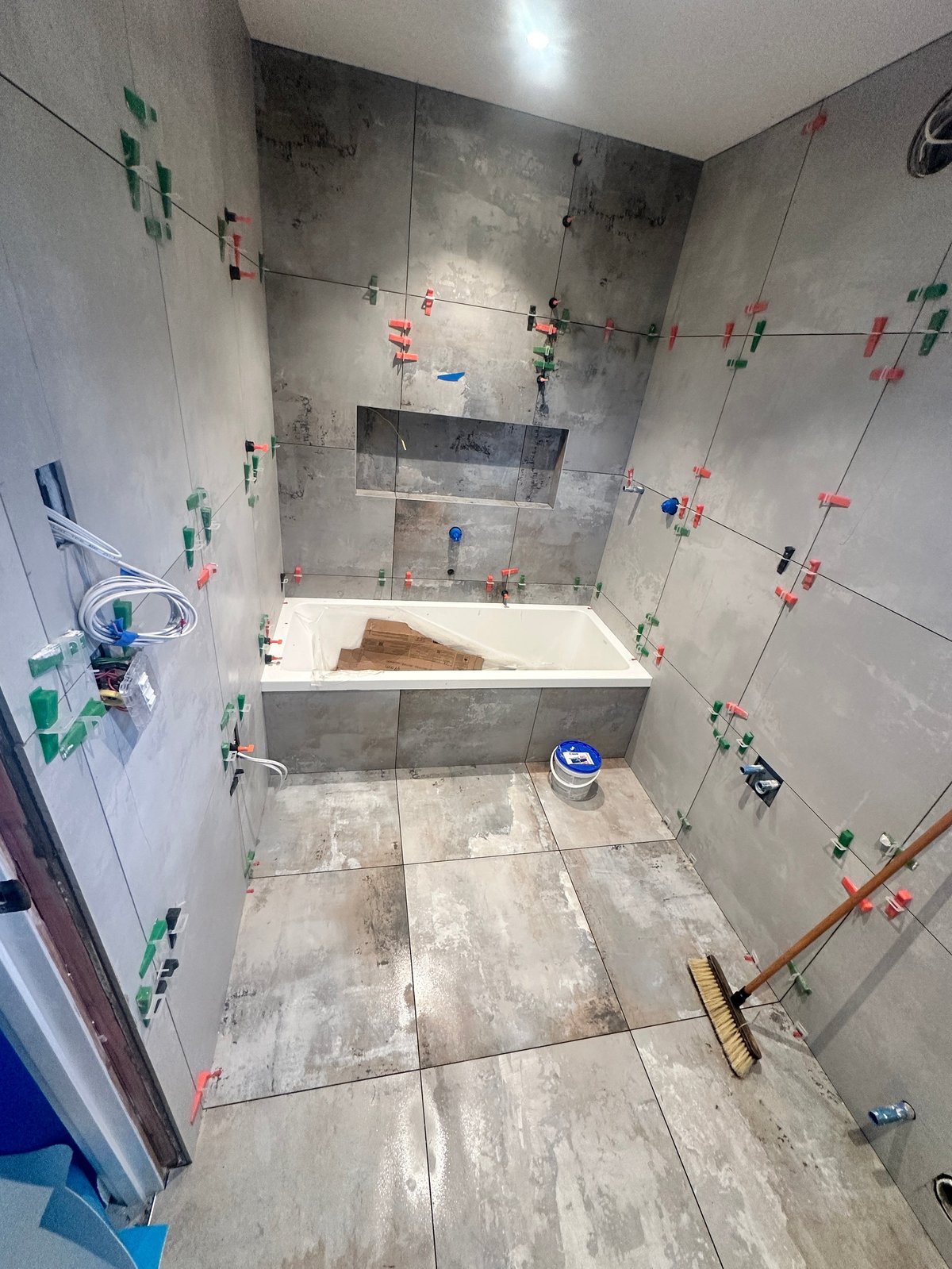 Bathroom under renovation with tile work in progress, showing a bathtub and floor tiling with construction markers and tools