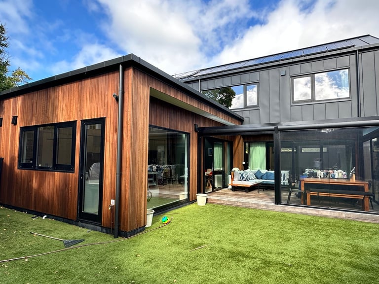 Architecturally designed timber and dark-clad homes in Auckland, with large windows and glass doors onto the lawn