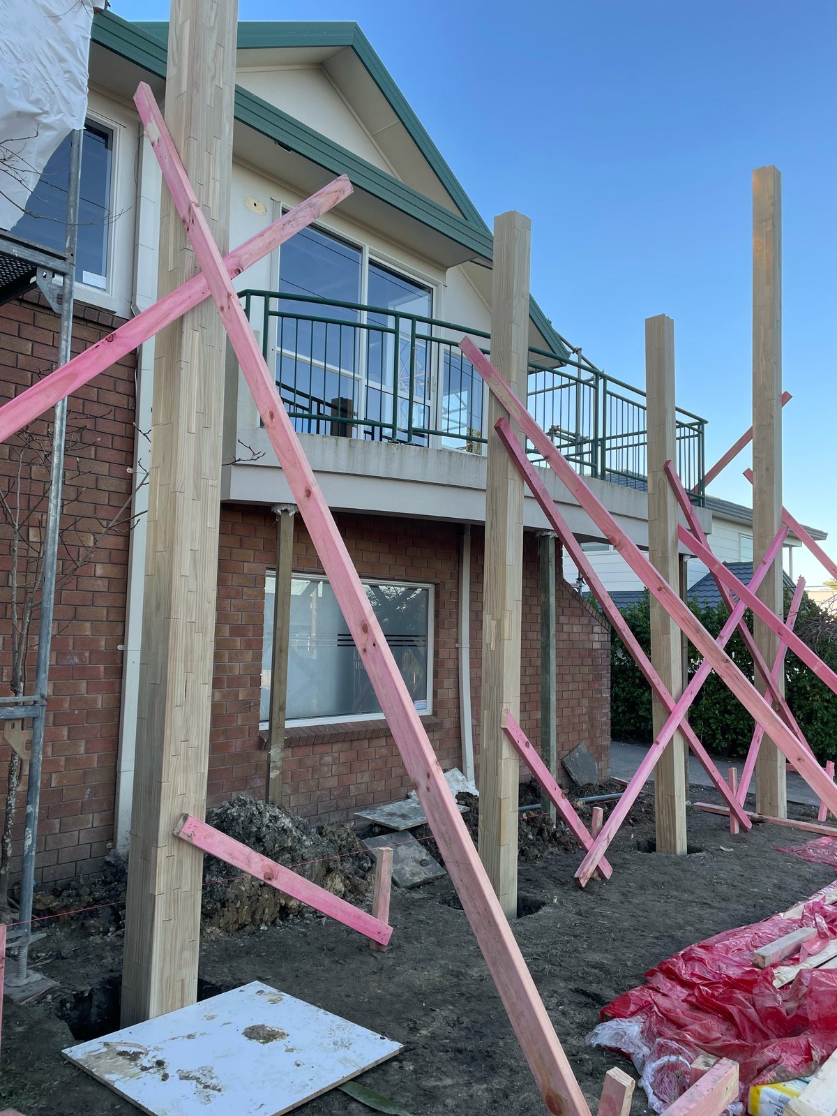 Brick house under construction with pink X-bracing supports on a new timber deck and extension frame