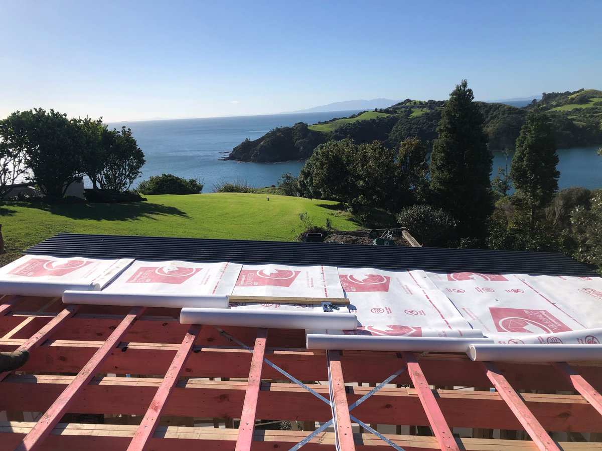Roof construction with insulation batts and breathable underlay, overlooking green hillside and coastal bay