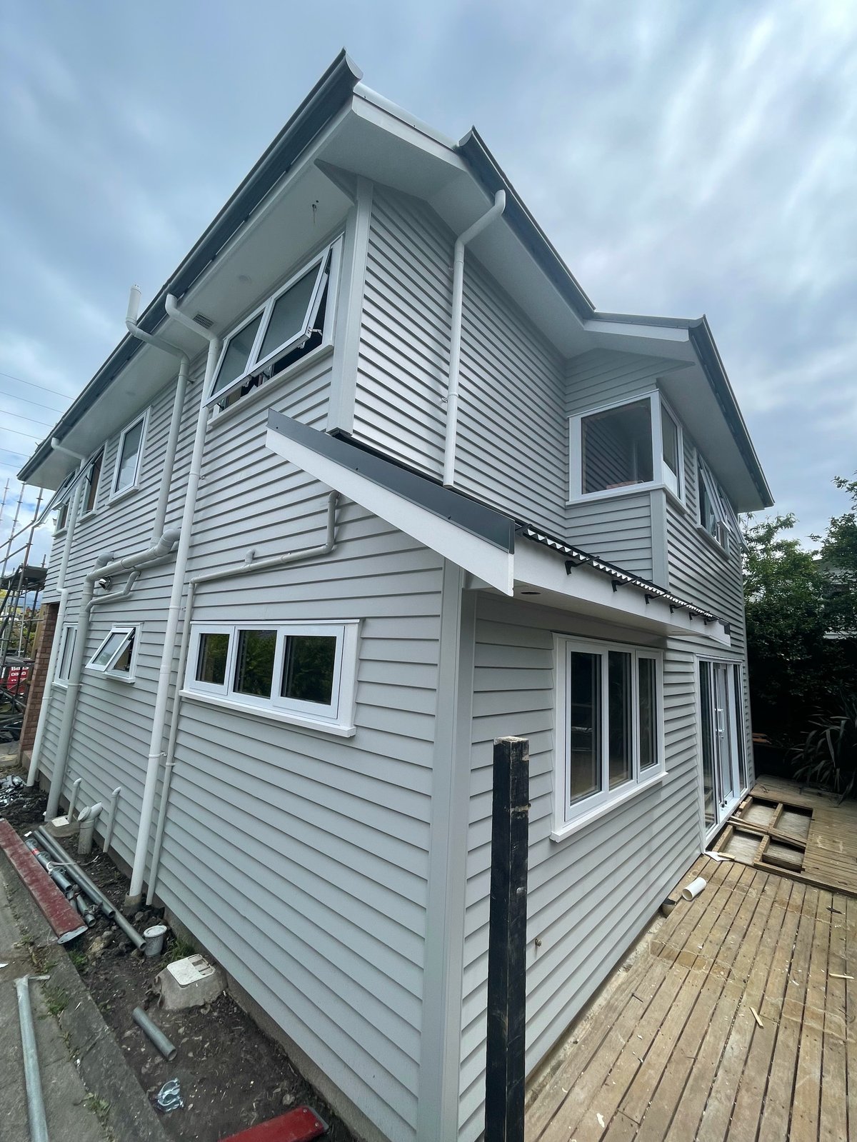 Modern two-storey house with light grey horizontal weatherboards, white-trimmed windows and an elevated deck