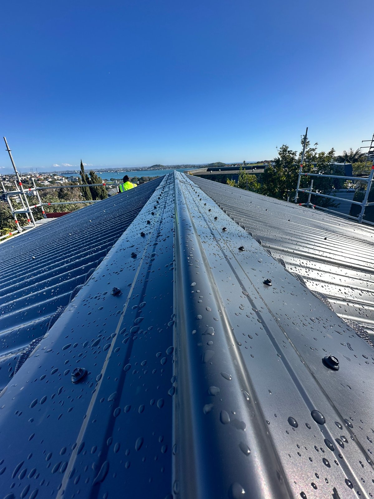 New corrugated roof ridge and fixings with rain beading on the metal, city and harbour in the distance