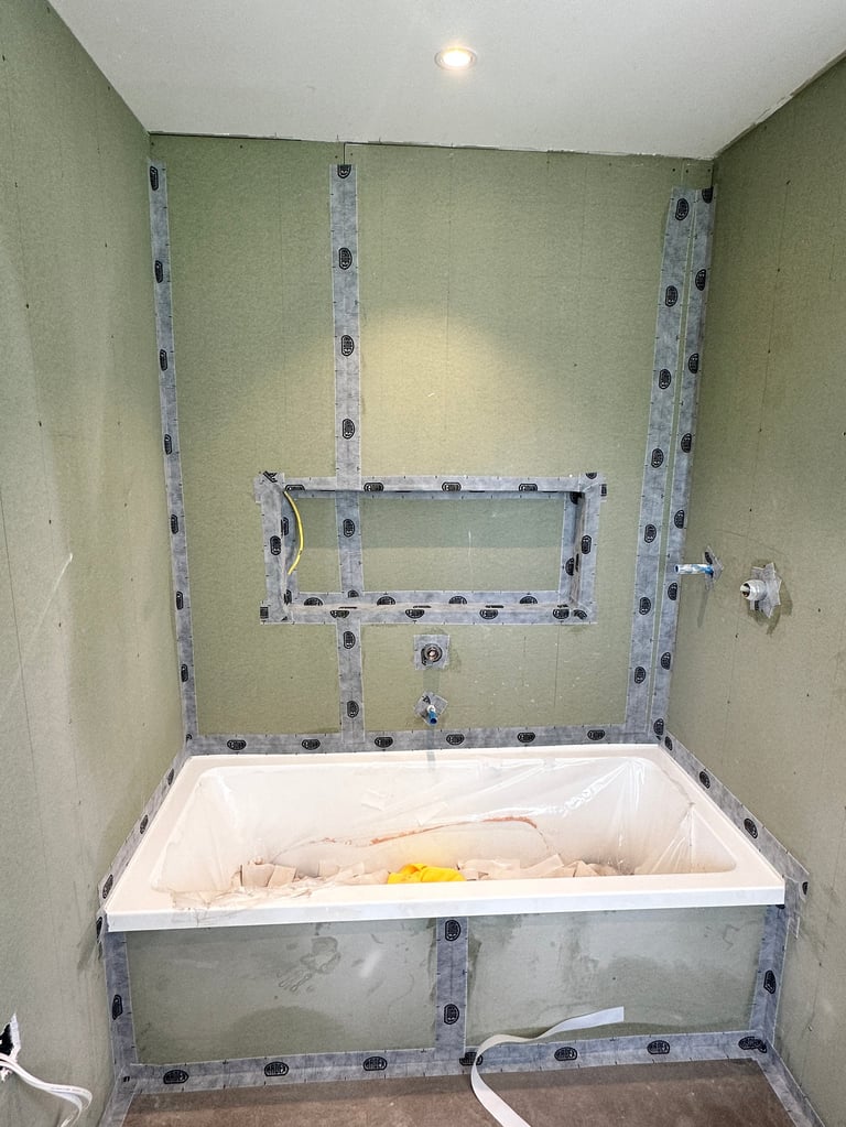 Bathroom under construction with white bathtub, drywall framing, metal studs, and holes for plumbing fixtures