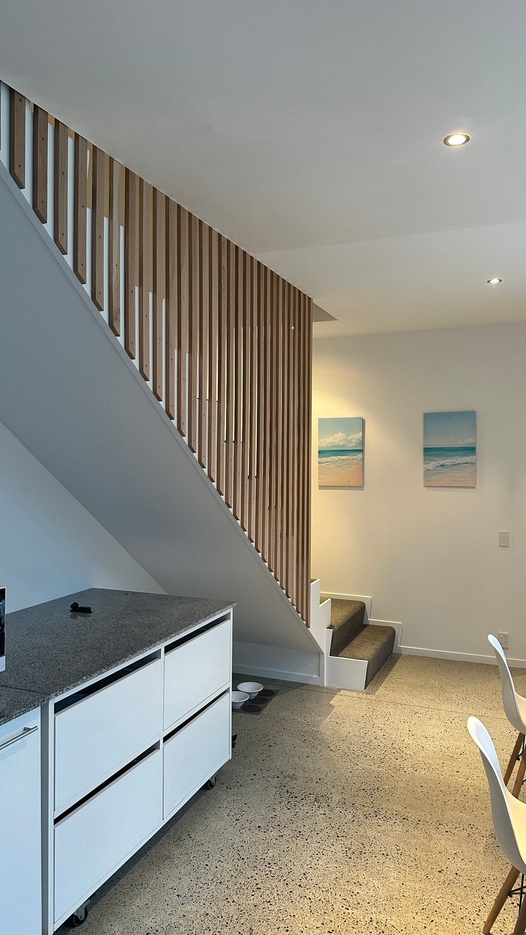Modern minimalist interior with floating stairs, wood slat railing, kitchen counter, beach artwork, and polished concrete floors