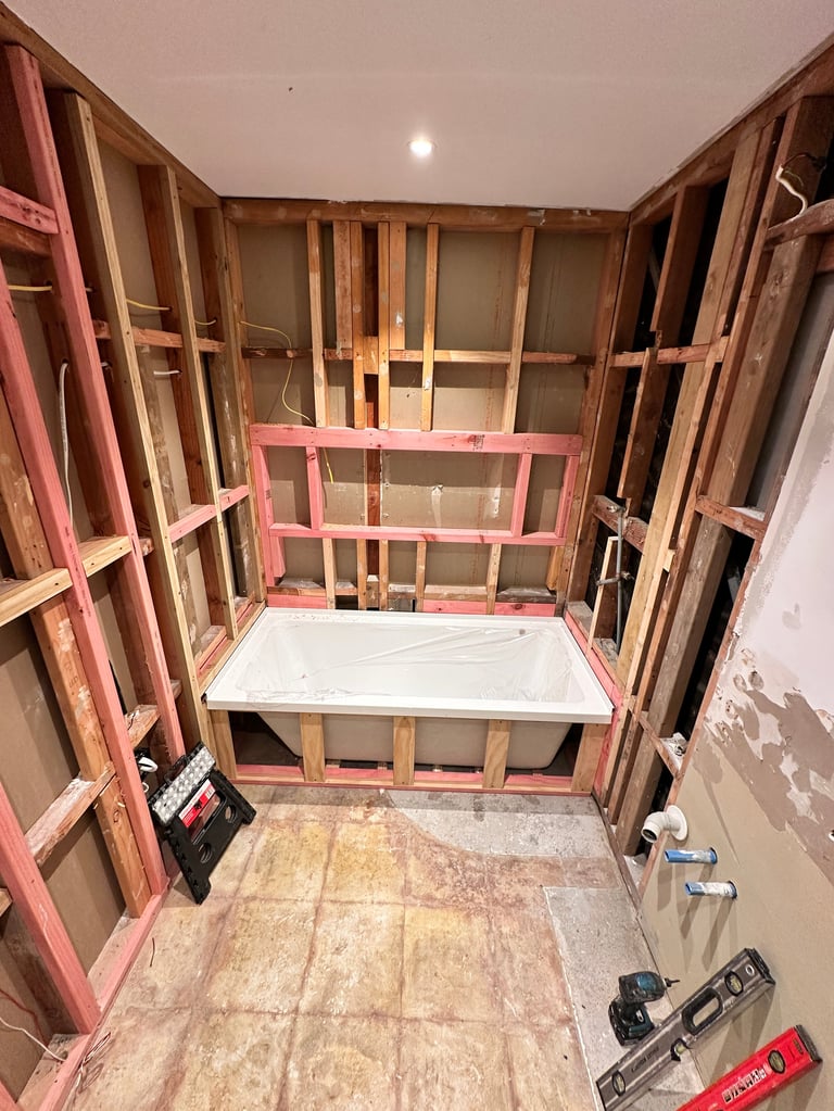 Construction site showing wooden framing and pink metal studs for a built-in bathtub installation in drywall