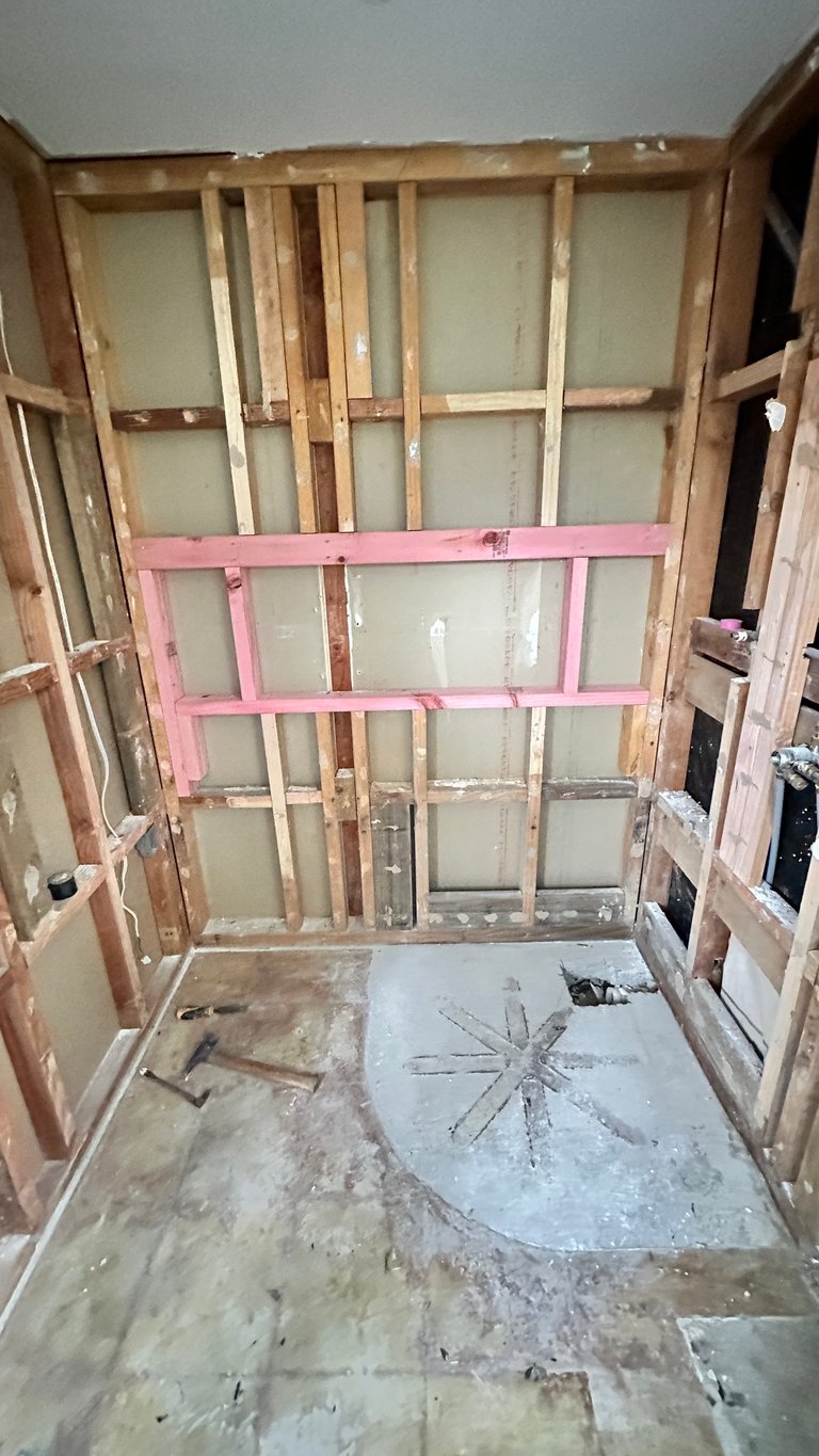 Unfinished bathroom interior with exposed wooden framing, drywall sheets, and pink painted studs during renovation