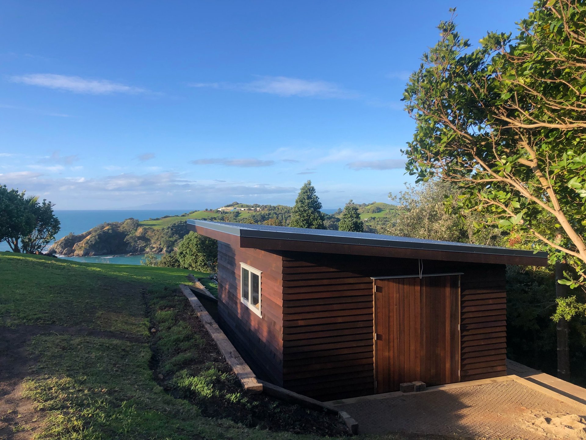 Modern cedar cabin on a Waiheke Island hillside with coastal bay and ocean views