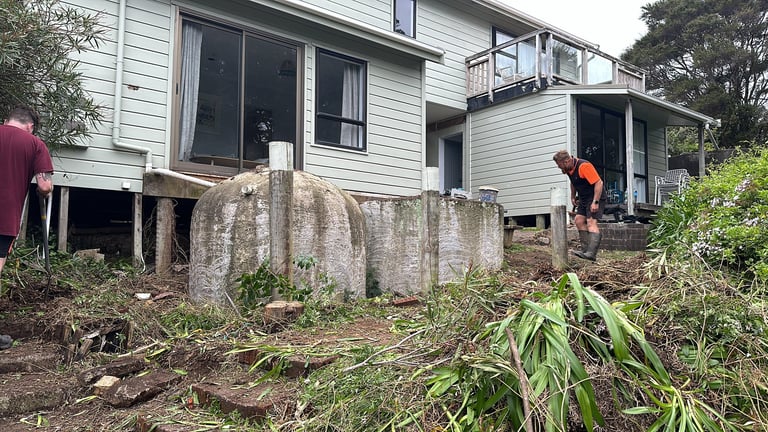 Raised house on concrete stumps with overgrown vegetation and people working on the property outside