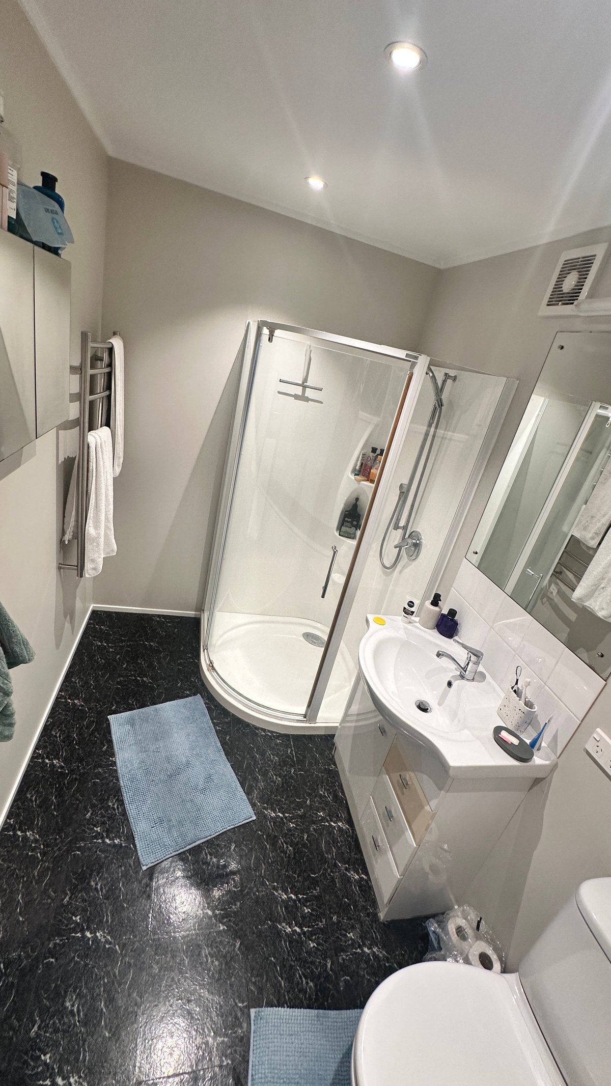 Modern bathroom with white walls, black marble floor, curved glass shower enclosure, white sink vanity, and white toilet