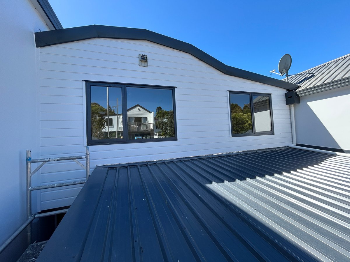 Modern white building with curved roof and dark blue metal roof sections featuring large windows and satellite dish