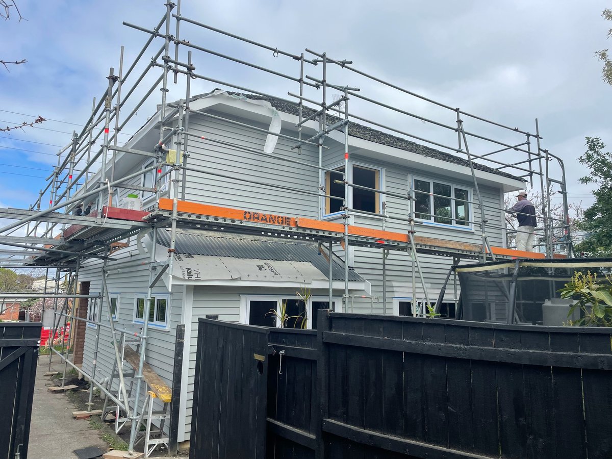 Two-storey house under renovation with metal scaffolding, orange safety barriers and black temporary fencing