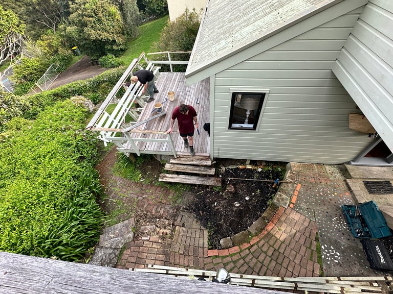 Aerial view of a gray house with white deck and patio, surrounded by green lawn and landscaping with brick walkway