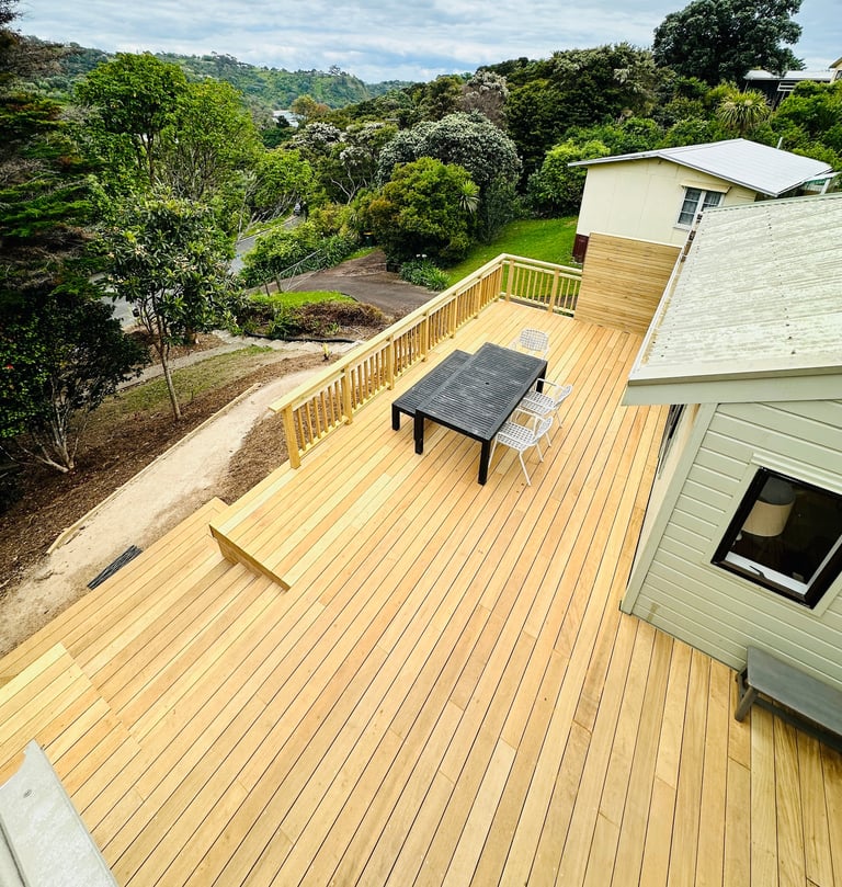 Elevated wooden deck with table overlooking lush green hillside landscape and modern house extension