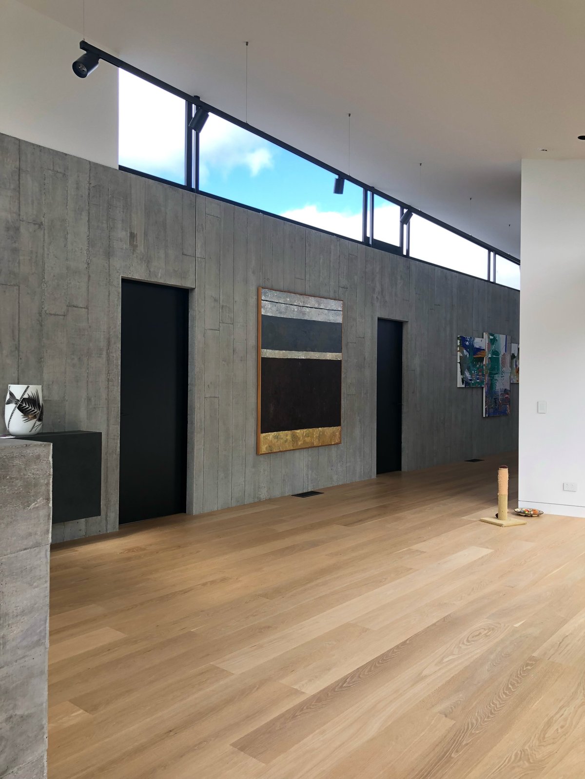Modern interior gallery with board-formed concrete wall, light oak flooring, black internal doors and high-level clerestory glazing