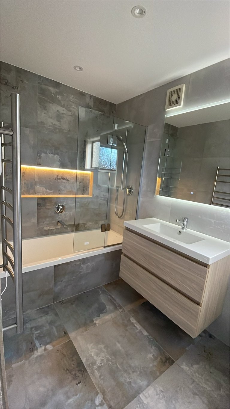 Modern bathroom with glass-enclosed shower, wooden vanity, white sink, and warm ambient lighting