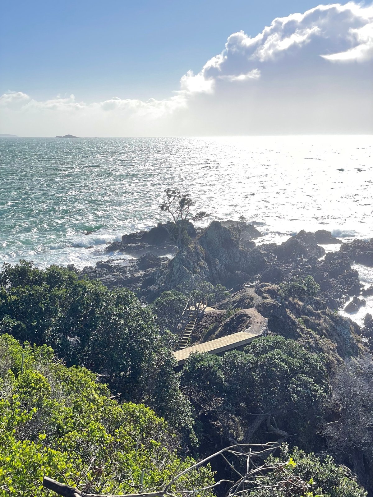 Coastal rocky outcrop with winding pathway overlooking turquoise ocean and sky with white clouds