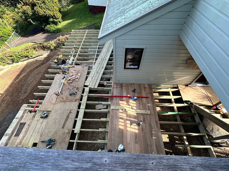 Construction of house deck and stairs with metal handrail and gray siding visible