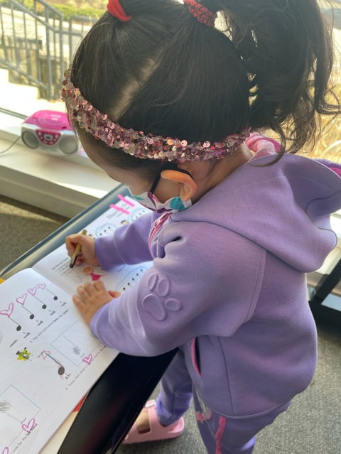 Child wearing purple hoodie drawing on worksheet
