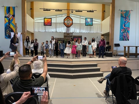 Children standing on church stage being photographed by audience