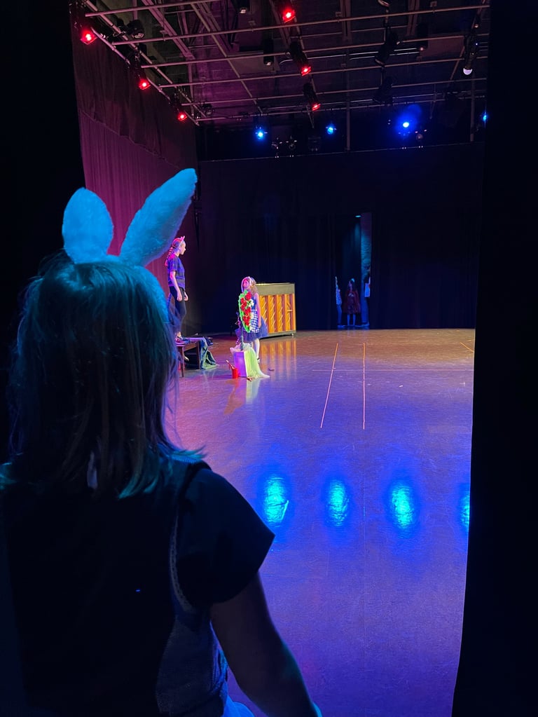 Audience member with bunny ears watches a colorful theatrical stage performance with neon lighting and performers