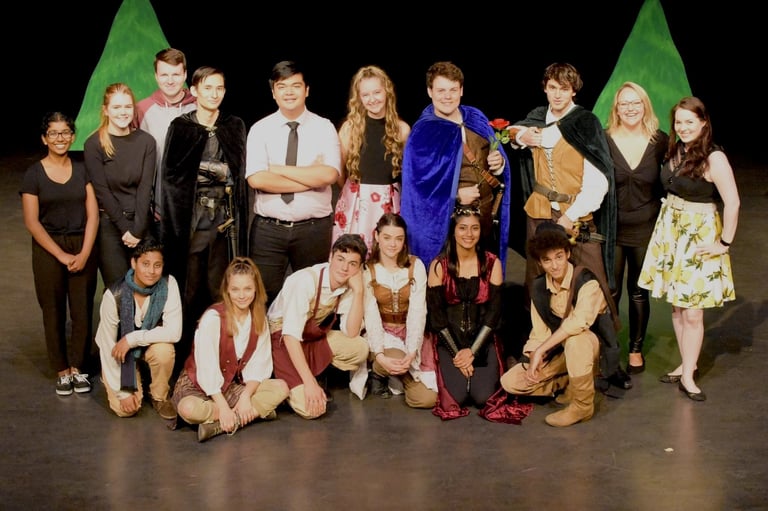 Large group of young performers posing together on a theater stage with green lighting backdrop