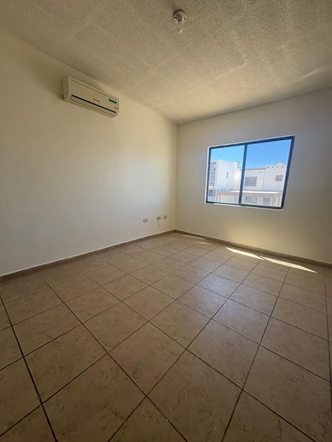Recámara vacía con piso de loseta, paredes blancas, ventana, minisplit en pared y foco de techo