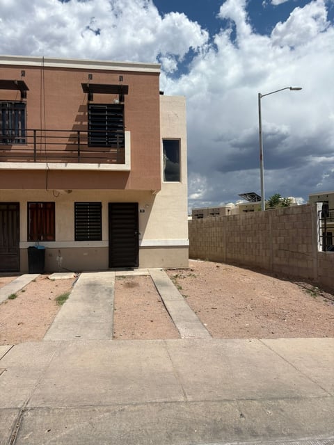 Fachada de la casa de dos pisos color beige con puertas y ventanas negras, barda perimetral y estacionamiento