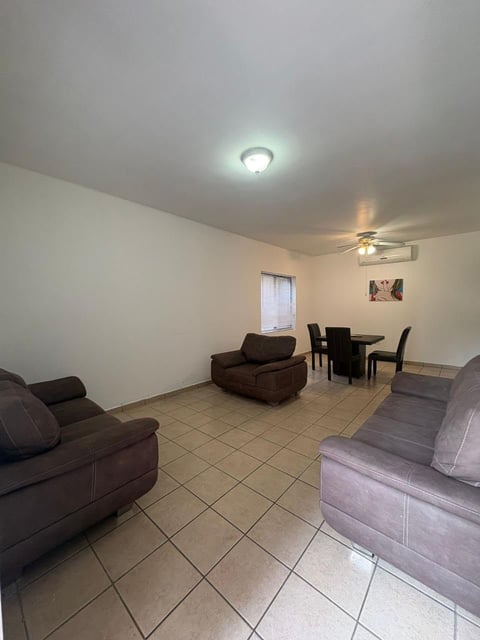 Sala amplia con piso de loseta, muebles color café y gris, ventilador de techo y comedor con mesa pequeña y sillas