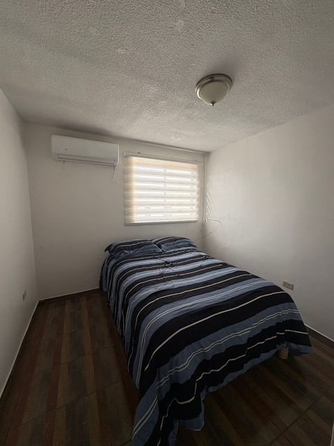 Recámara con cama individual, ventana con contraventanas y minisplit
