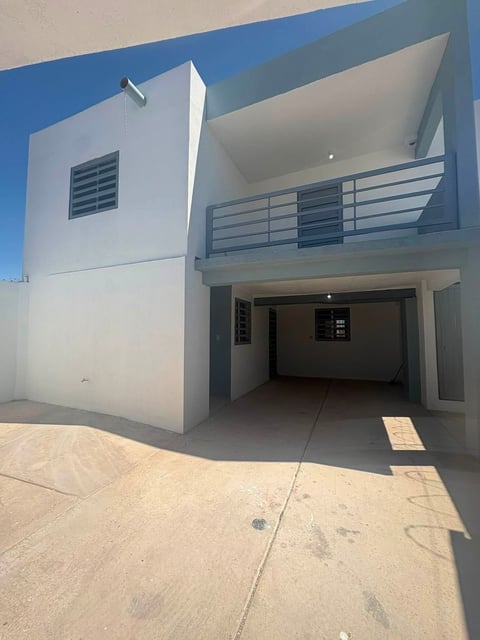 Casa moderna blanca con azul de dos pisos, cochera abierta y balcón cubierto sobre pavimento