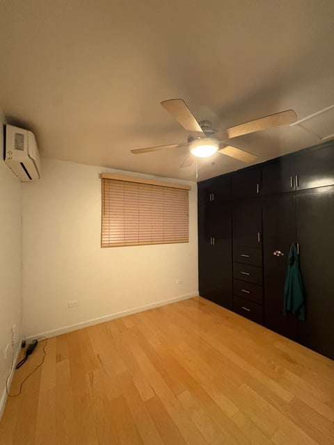 Recámara con clóset negro grande, piso de madera, ventana con persianas y minisplit