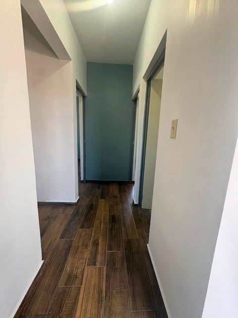 Pasillo angosto con paredes blancas, piso de madera oscura y dos puertas cerradas a ambos lados