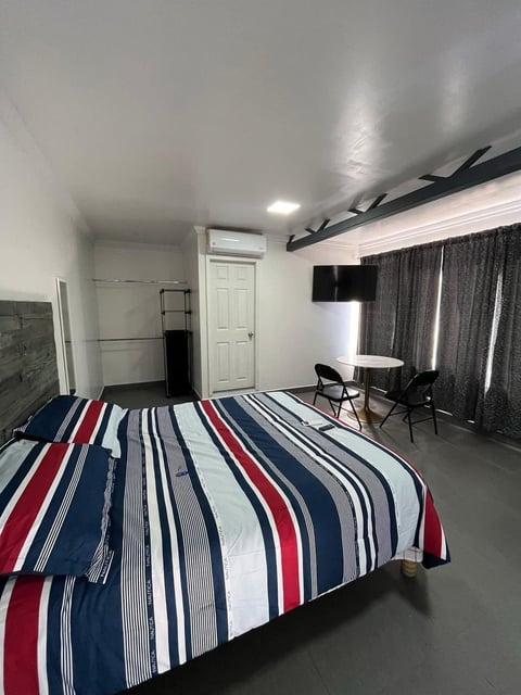 Recámara con cama, ropa de cama rayada, escritorio y cortinas oscuras