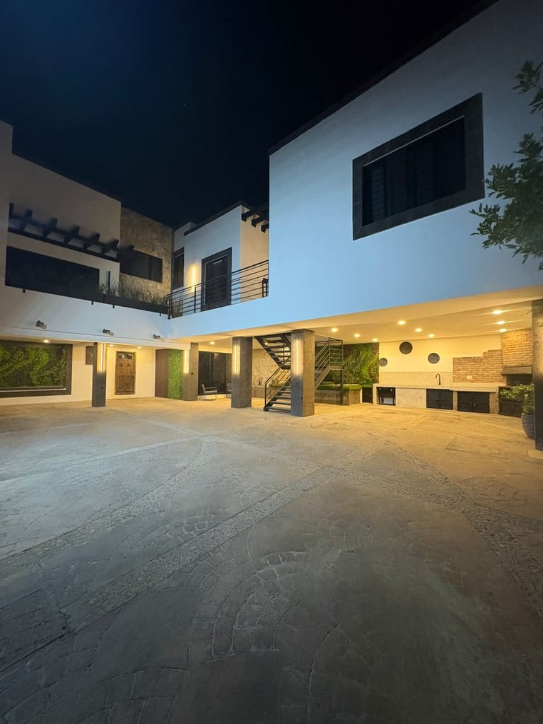 Modern two-story house with white and blue facade, illuminated courtyard, spiral staircase, and greenery at night