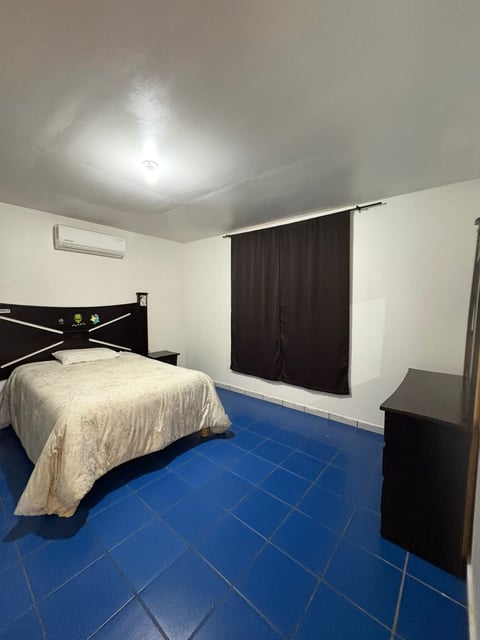 Recámara moderna con cama negra, edredón crema, cortinas oscuras y piso de loseta azul