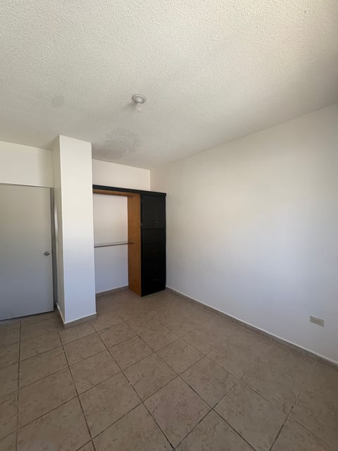 Interior vacío con piso de loseta beige, paredes blancas, estante empotrado y marco de puerta de madera