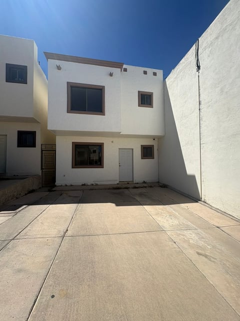 Fachada de townhouse blanco moderno de dos pisos con patio pavimentado bajo cielo azul