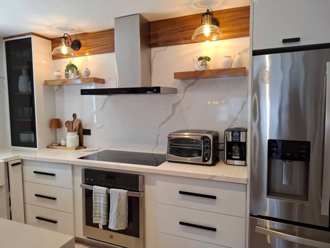 Cocina blanca moderna con backsplash de mármol, electrodomésticos de acero, estantes de madera y lámparas colgantes